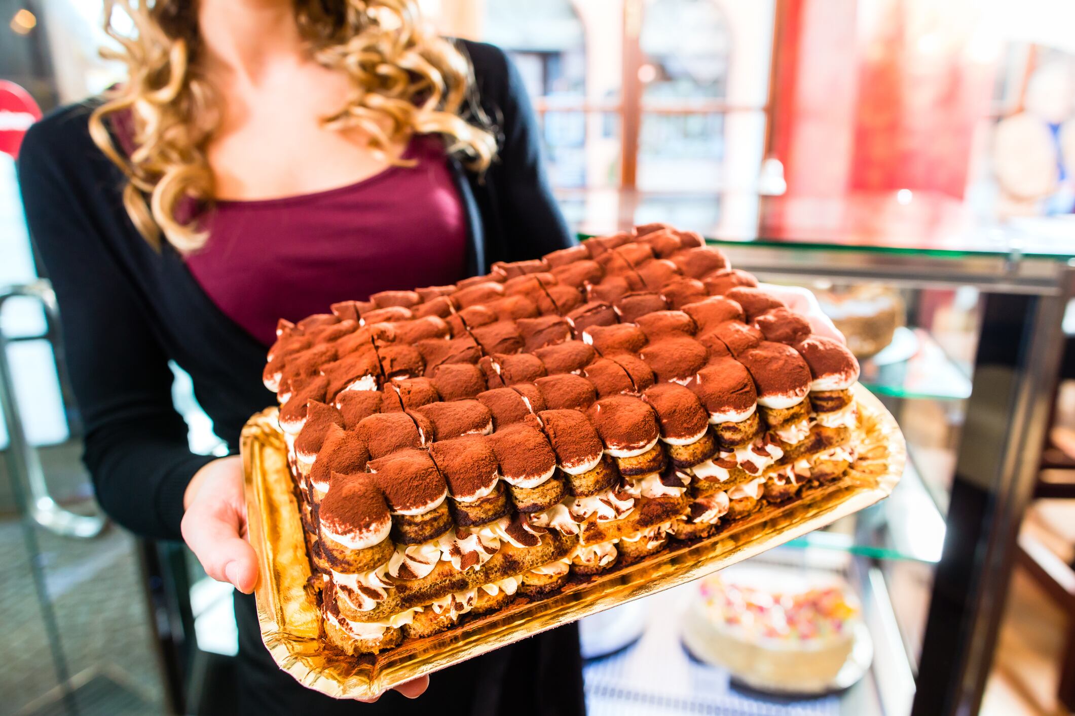 Female confectioner presenting tray of cake in bakery or pastry shop