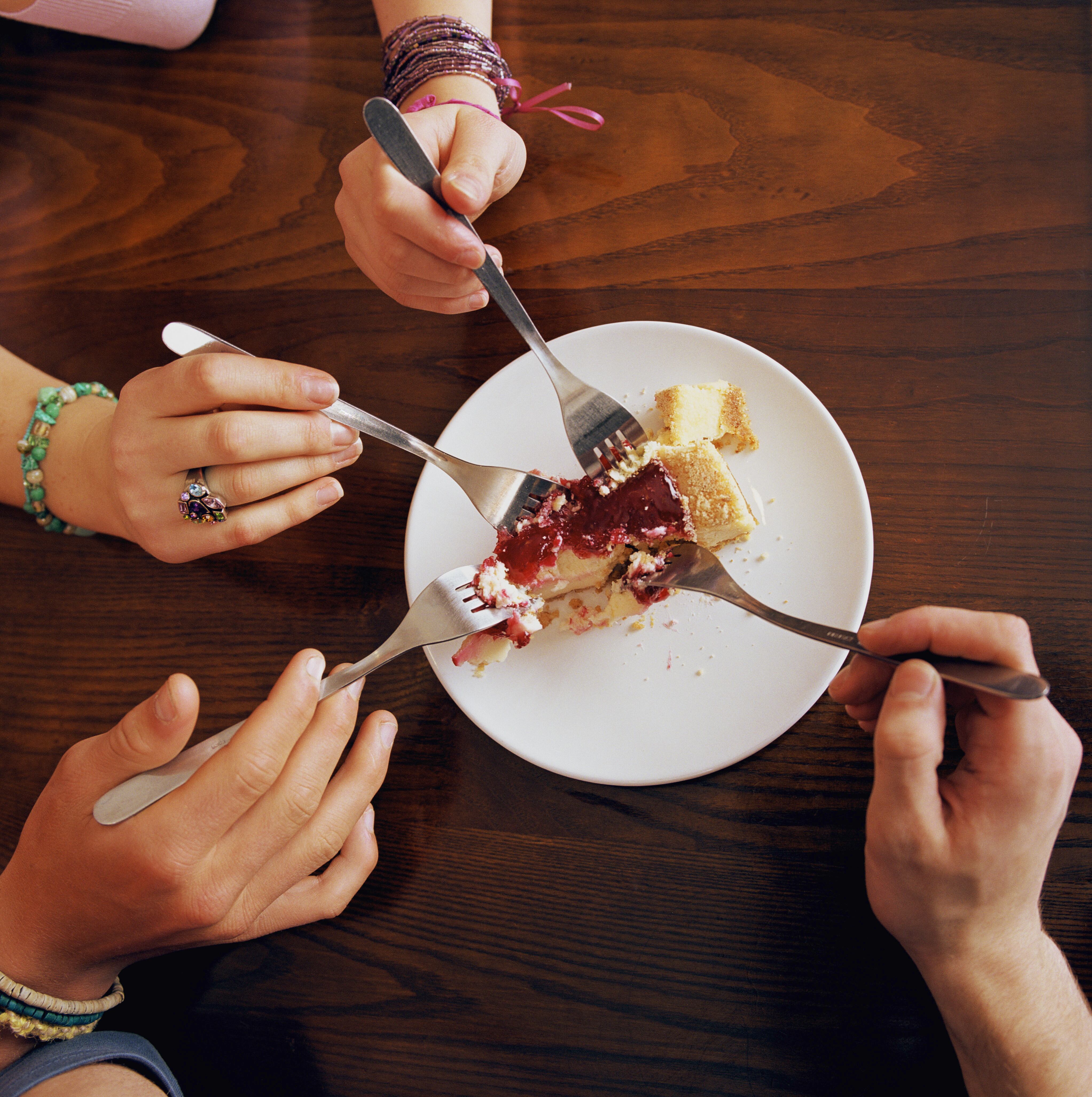 Three teenagers (16-18) and young man sharing cheesecake, close-up