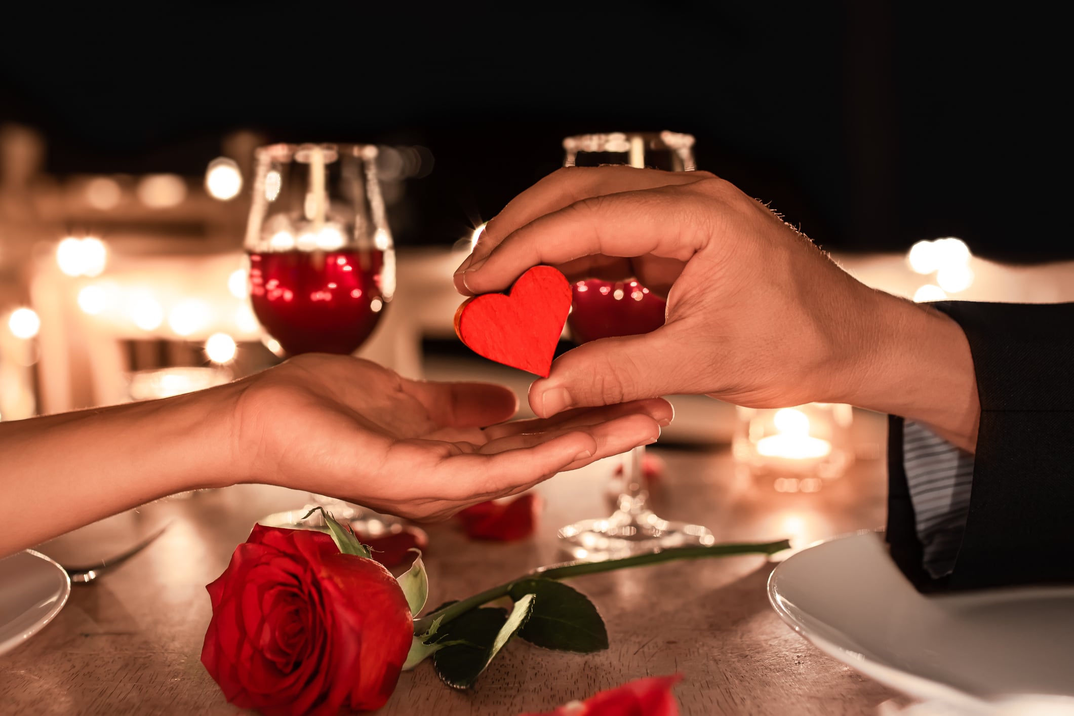 Romantic candlelight Valentine's dinner setting. Man giving woman a heart gift of love.