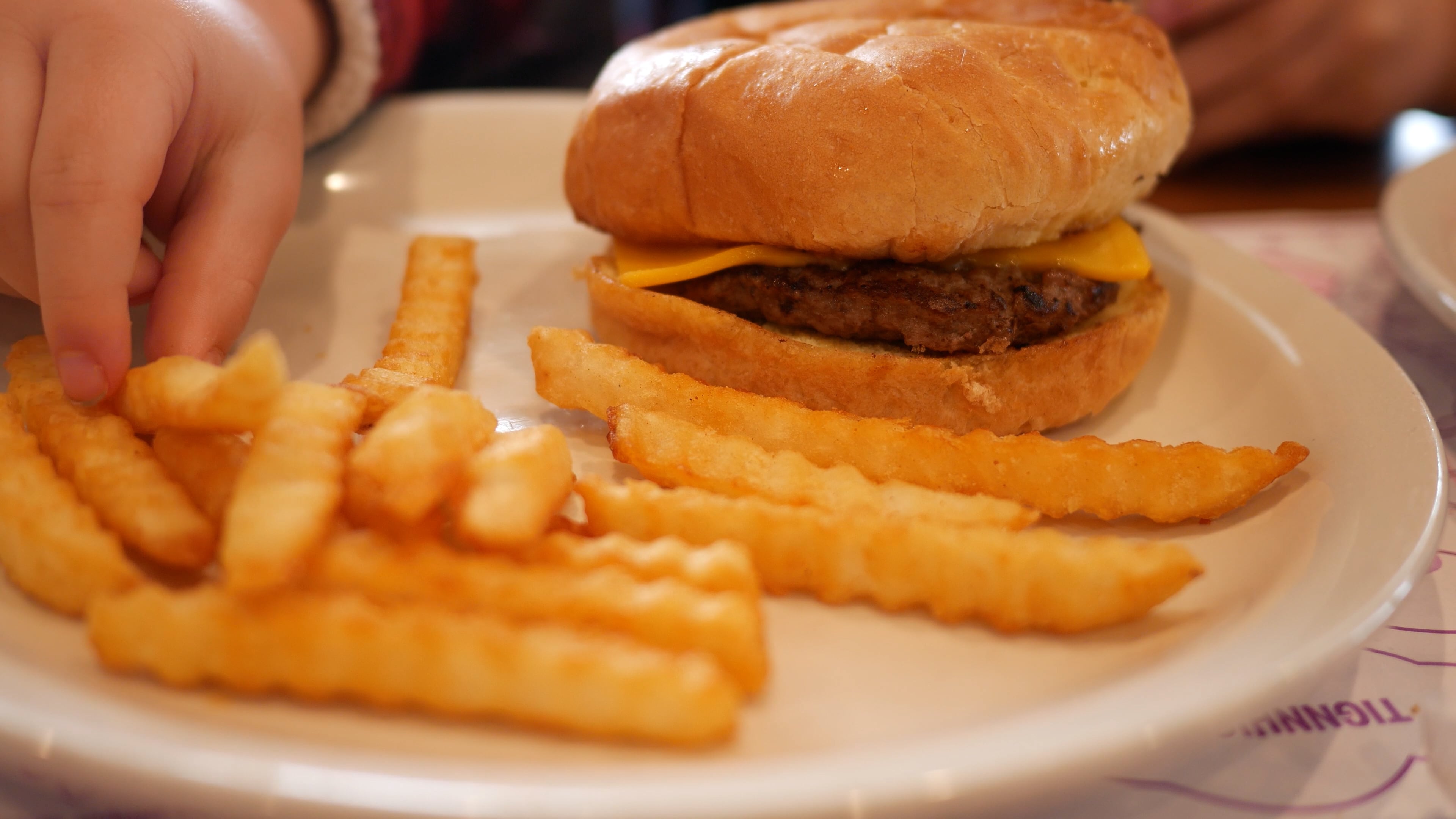 Toddler grabs French Fry on Plate with Cheeseburger