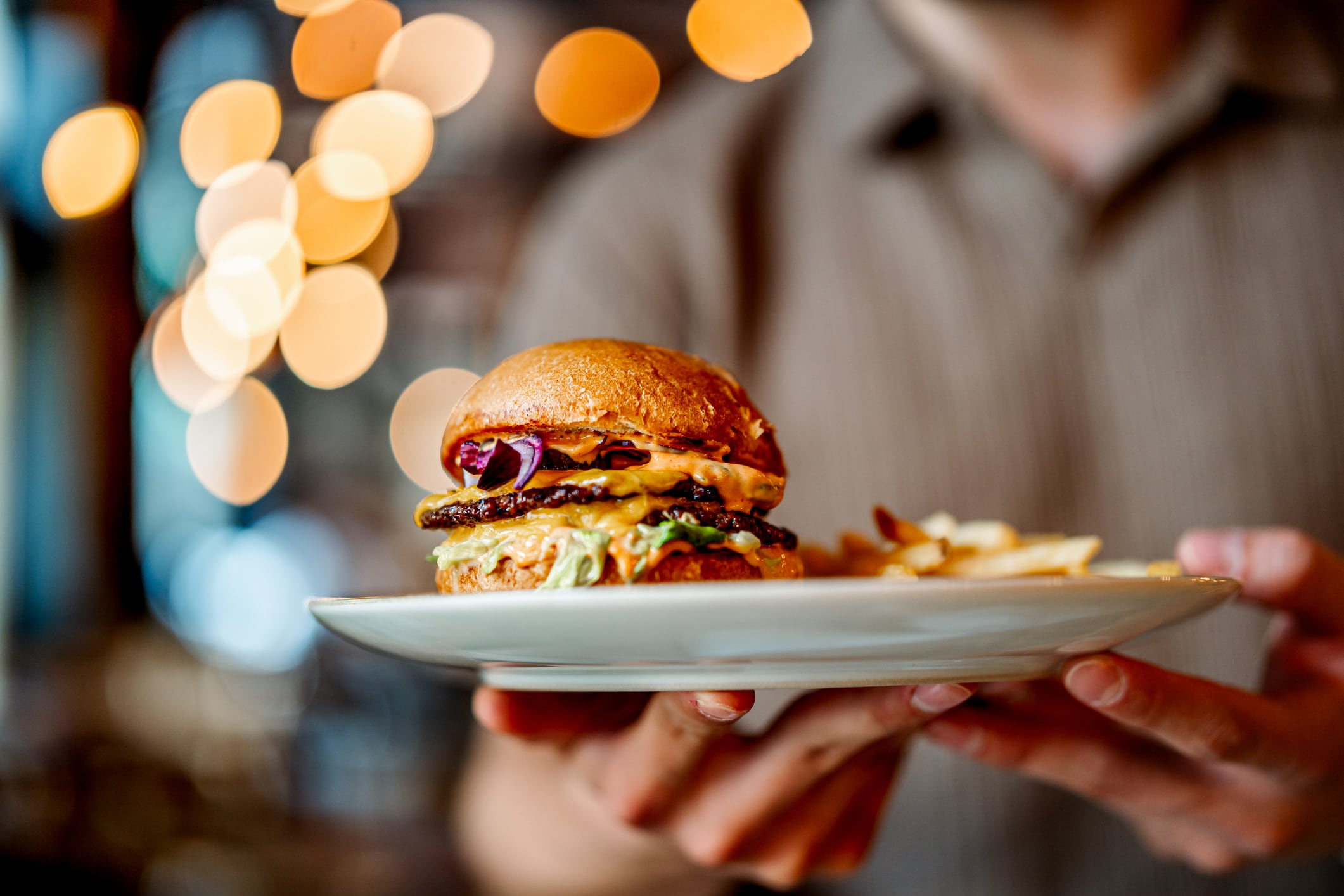 Waiter presenting a delicious double patty hamburger with cheese, fresh vegetables, and crispy fries in a casual restaurant setting