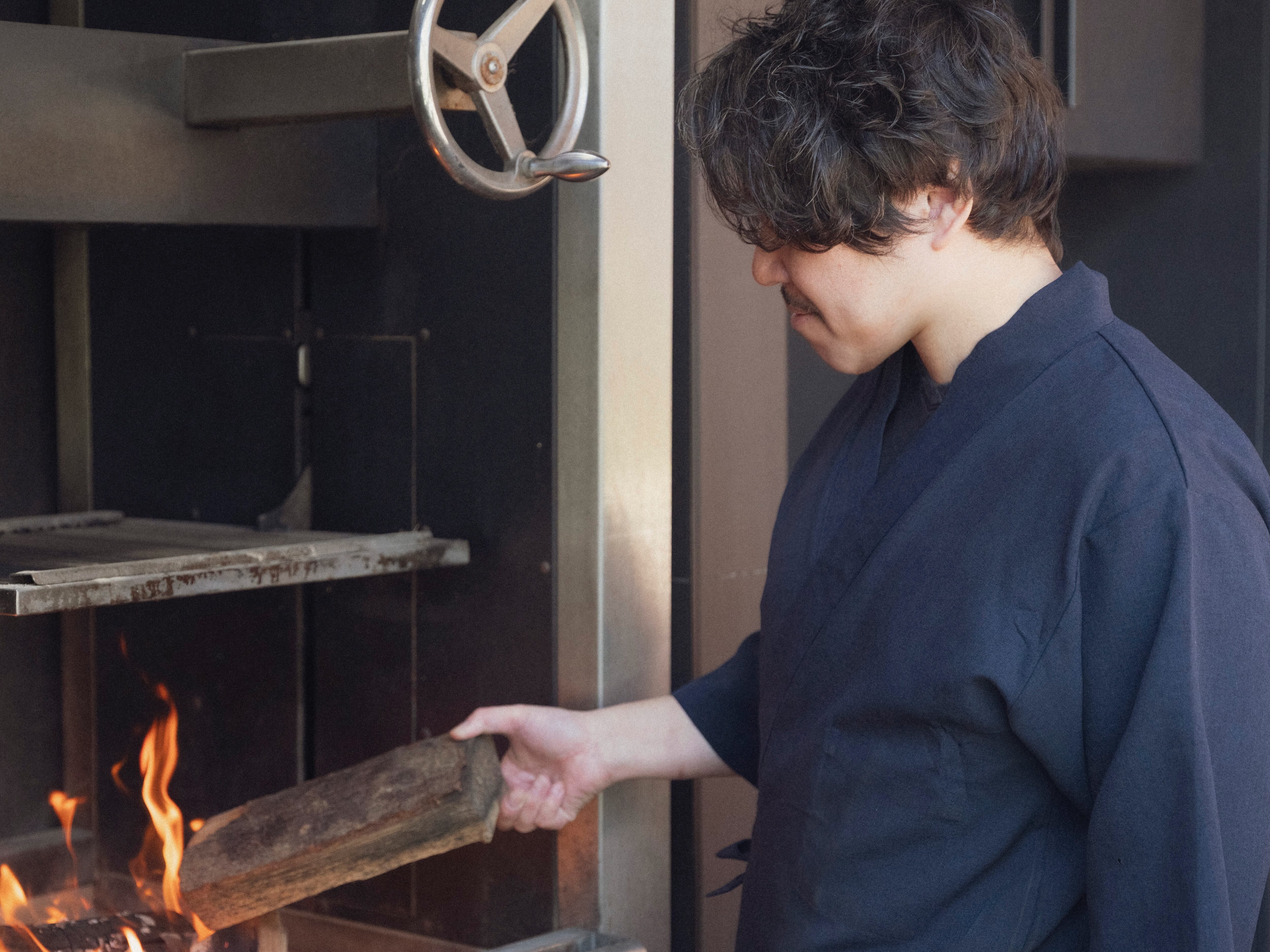 Chef Daisuke Shimoyama burning wood on a grill