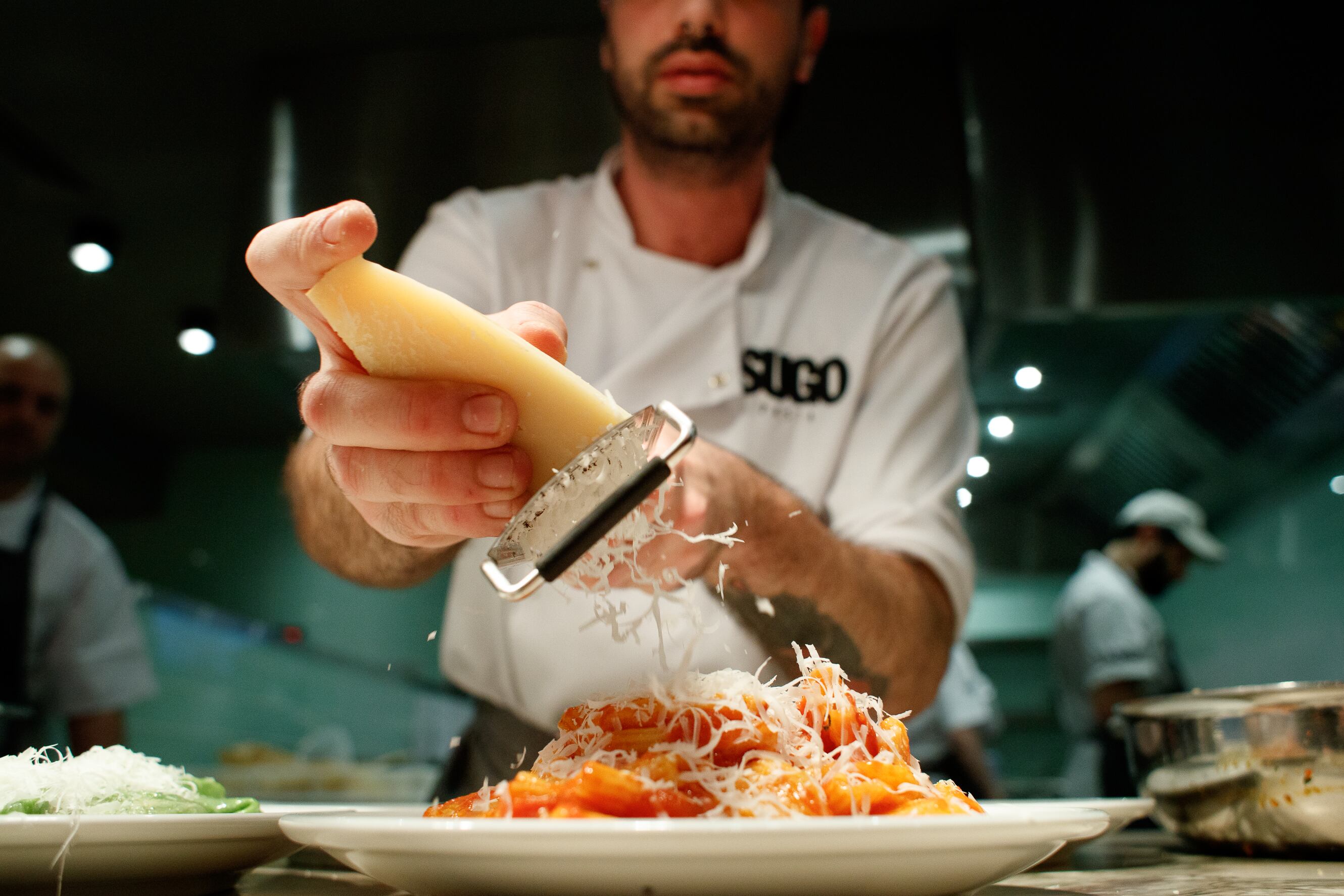 Someone grating cheese over a plate of pasta at Sugo Pasta