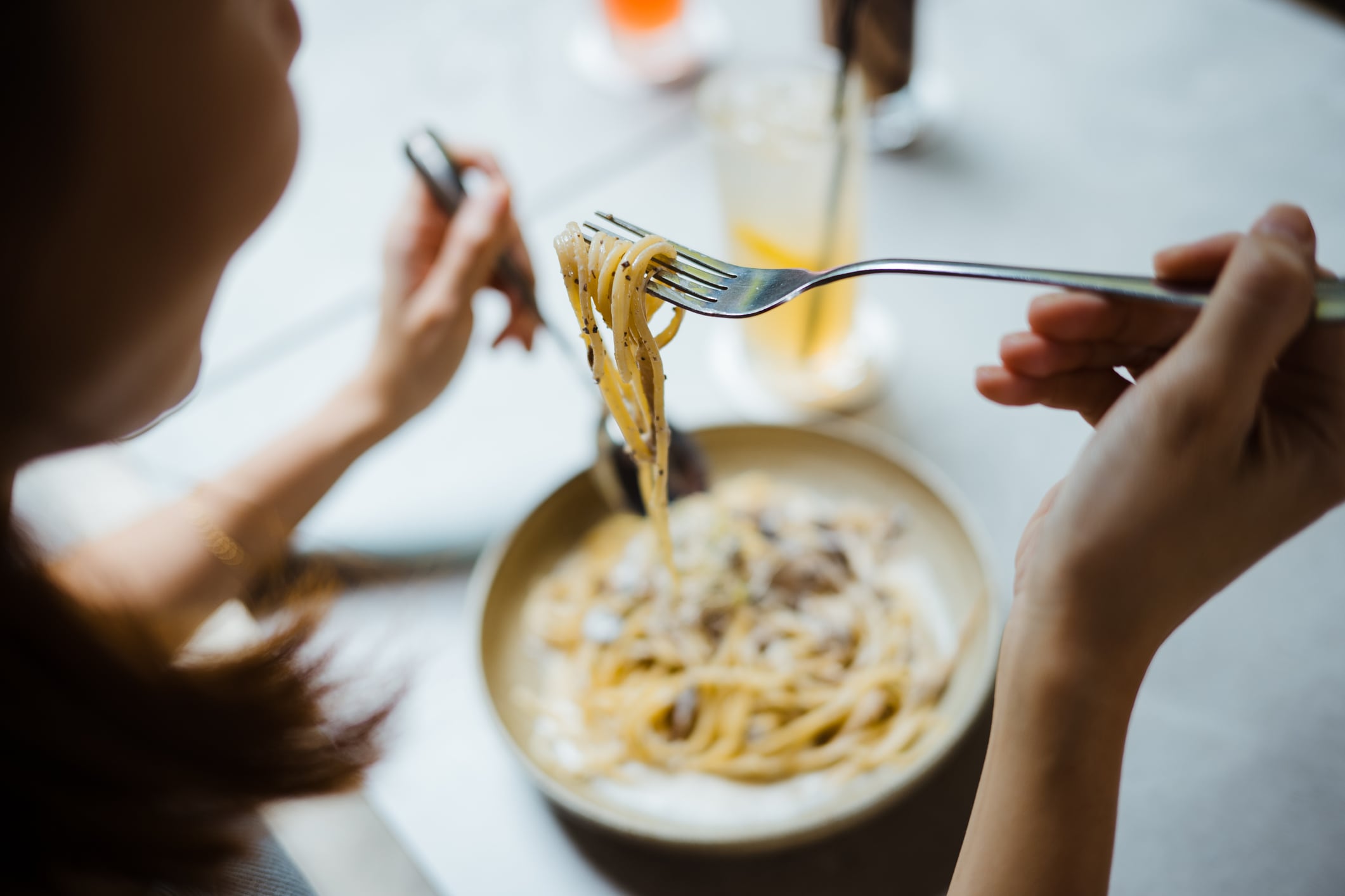 Rear View of a woman using spoon and fork to eat carbonara spaghetti on table