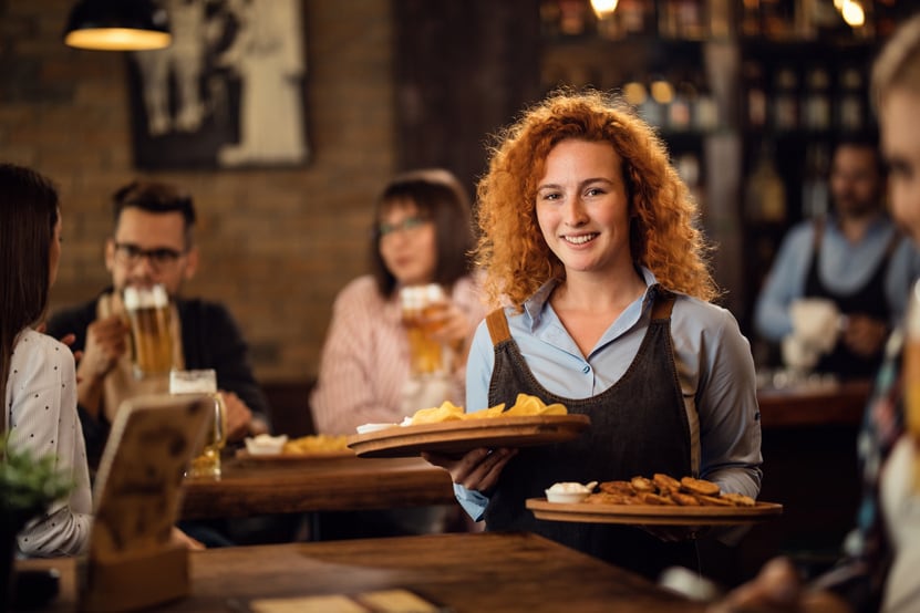 Happy redhead waitress serving customers in a restaurant and bringing food at their table.