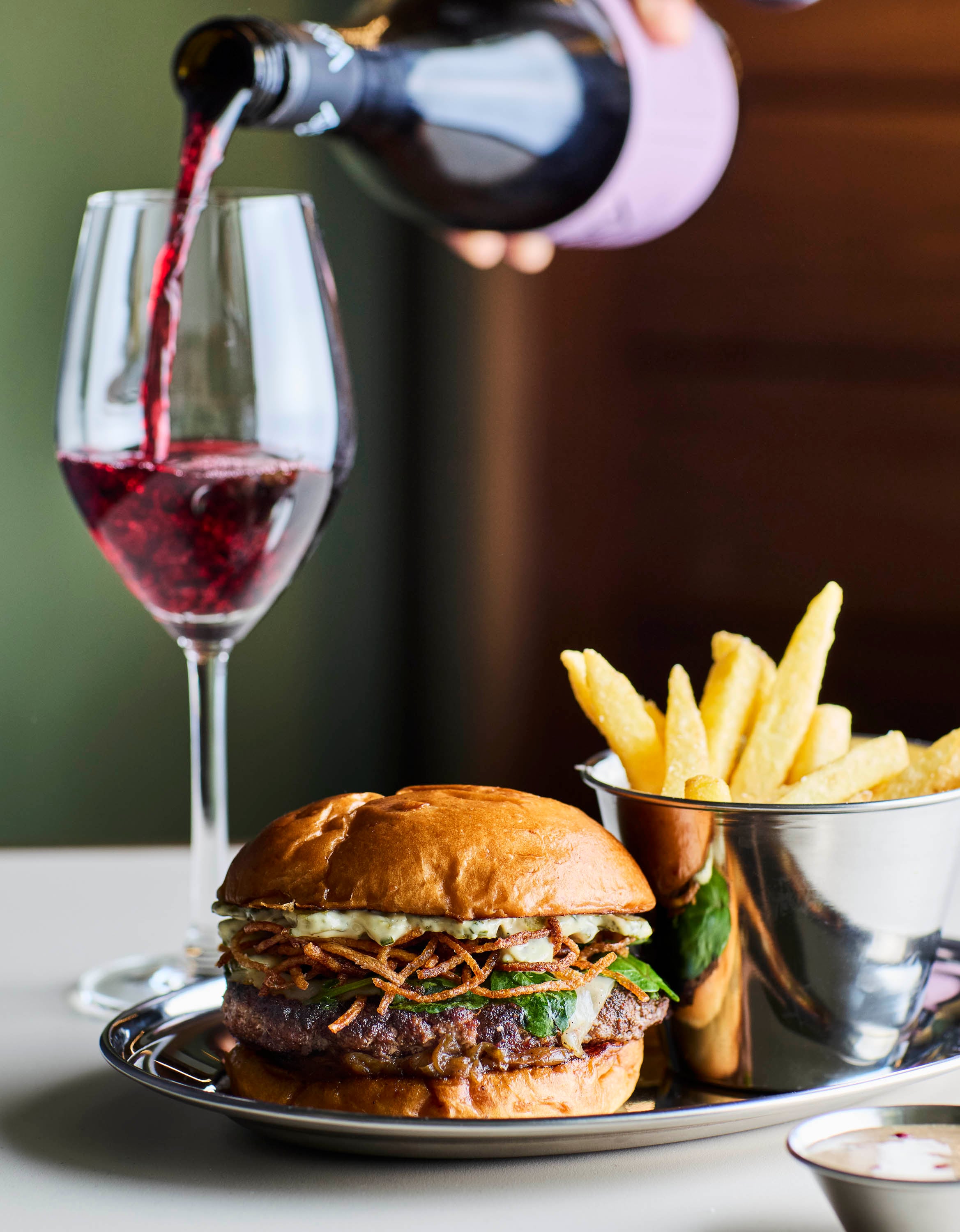 A burger a heard served with fries and a glass of red wine