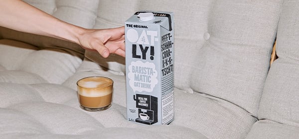Hand grabbing Oatly carton next to a coffee