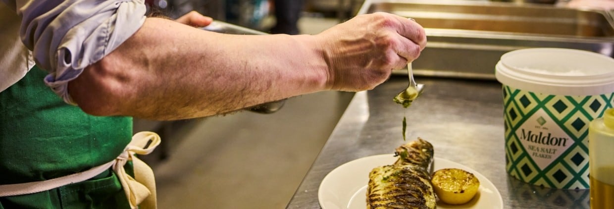 Chef sprinkling salt onto plate of food